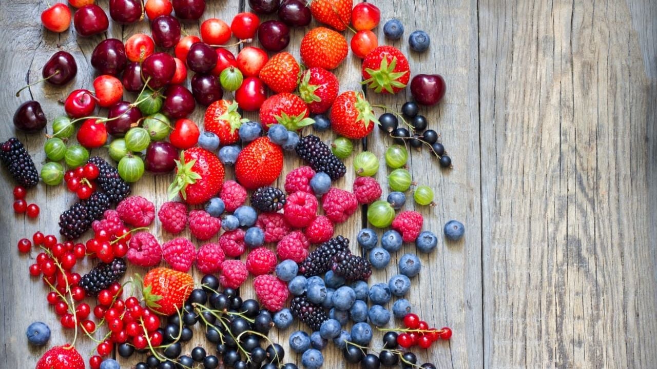 A collection of mixed berries, cherries and grapes on a wooden cutting block