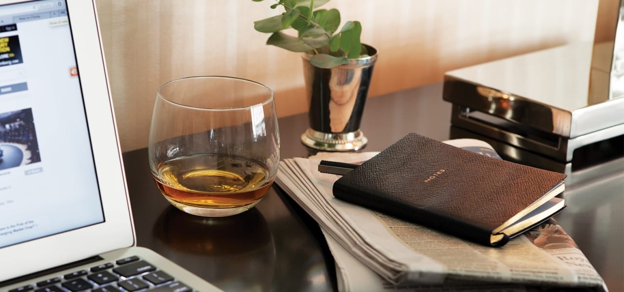 A glass of whisky and a leather notebook on a table at The Benjamin Hotel NYC